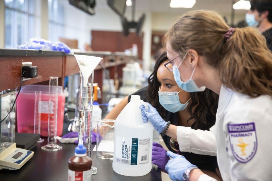 Two student pharmacists compound hand sanitizer.