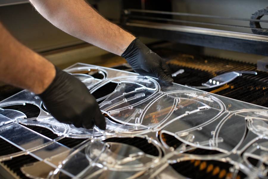 Two hands holding face shield materials while being cut on machinery in the College of Engineering. 