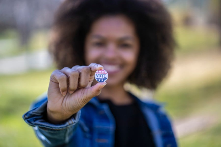 Woman holding a "Vote" pin