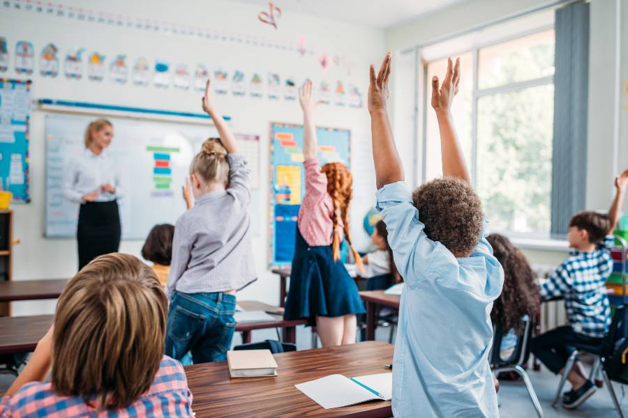 photo of student in a classroom raising their hands