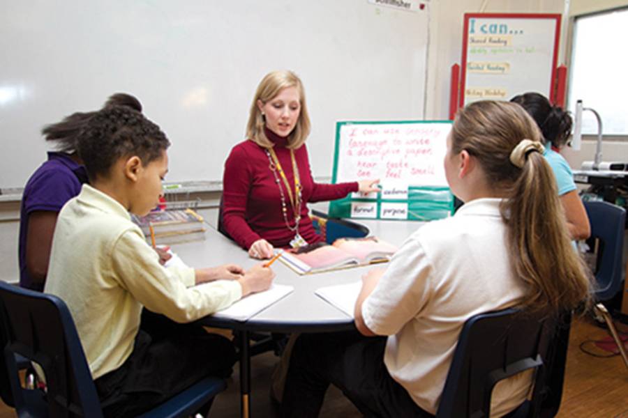 Female teacher sitting at table with elementary school students