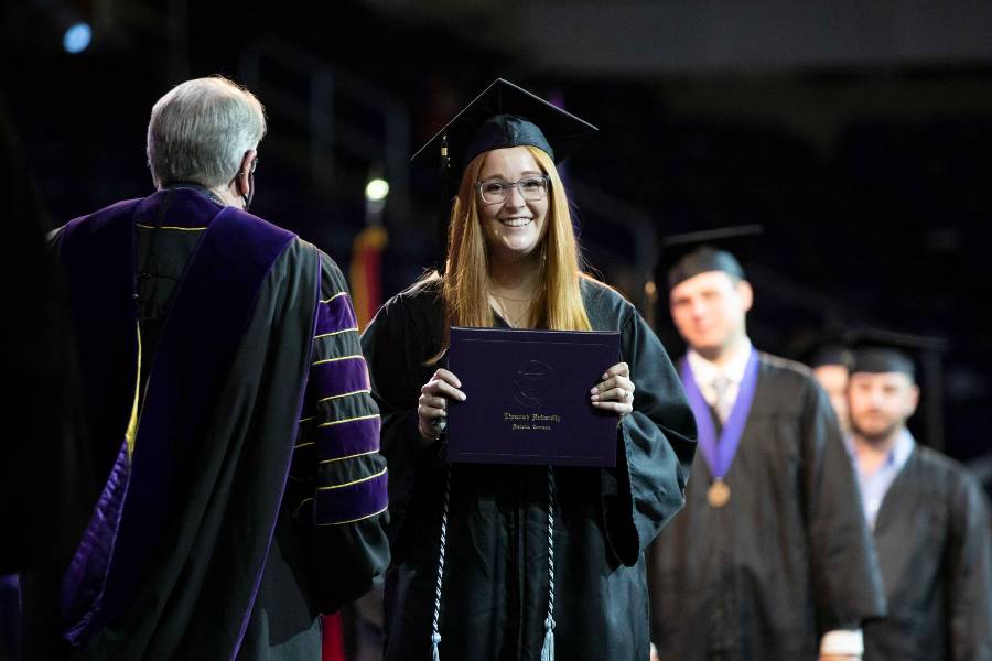 Smiling student crosses the stage with diploma