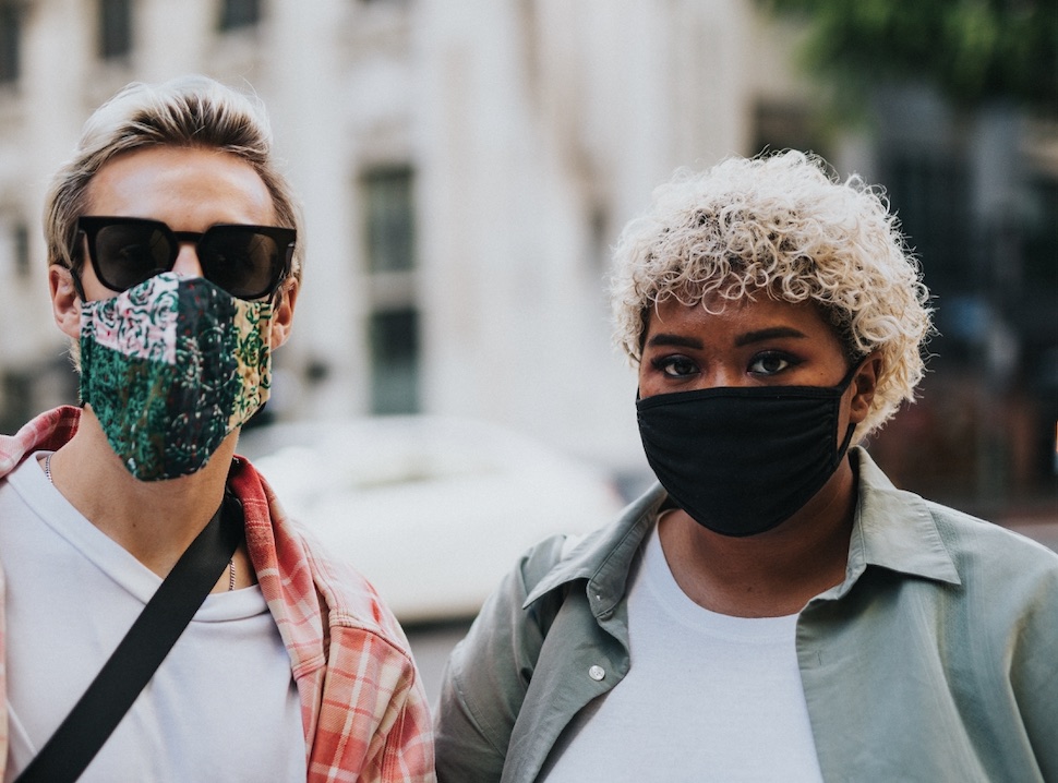 Two people look at the camera with masks on in an urban setting