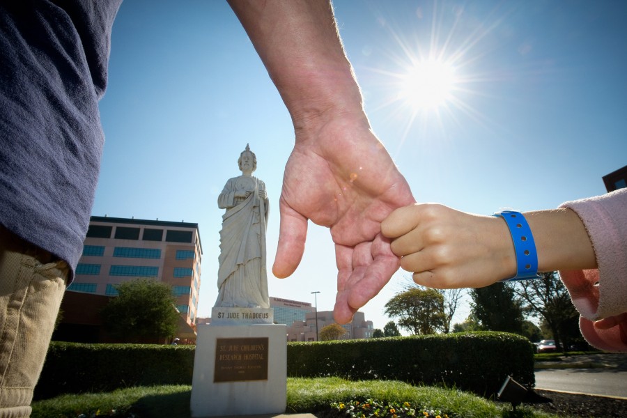 Patient holding parent's hand near statue of St. Jude.
