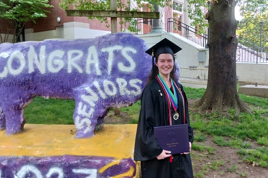 Anna Adams dressed in regalia standing next to bison statue pained "Congrats Seniors"