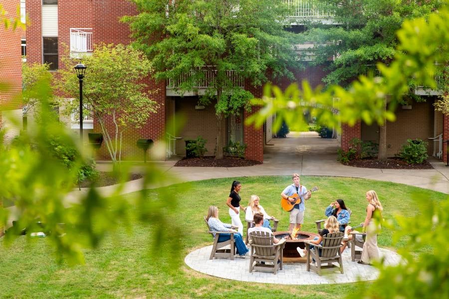Students in the courtyard of a dorm playing the guitar.