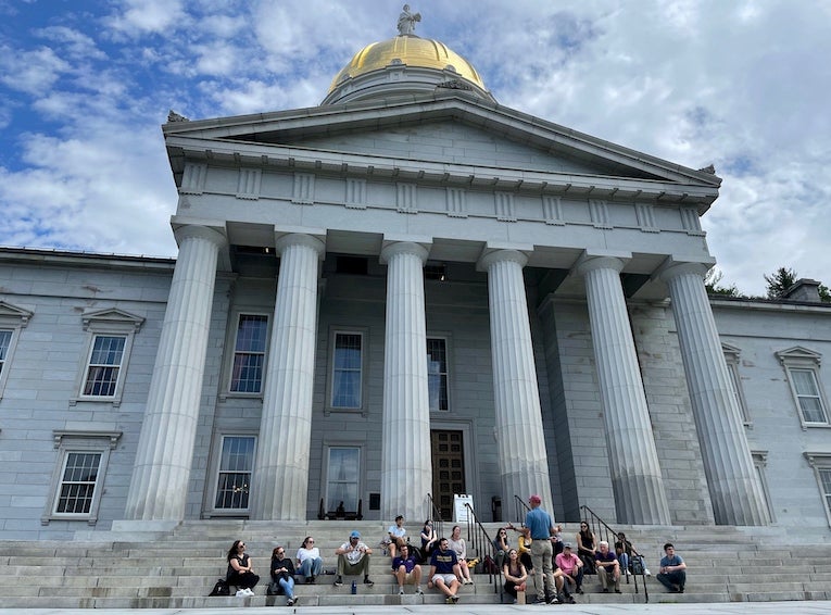 Students sit on steps of government building with tall columns as they learn