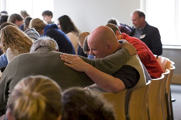 A group of men in a classroom pray with one another