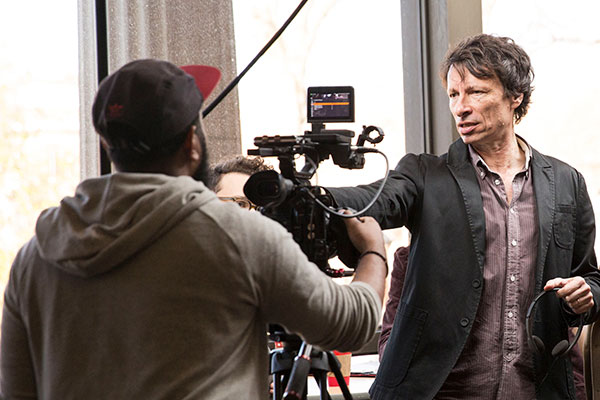 A professor points towards a student as another student records the interaction on a mounted camera