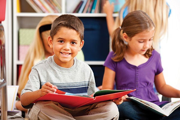 A young child looks forward as he holds a book open in his hands