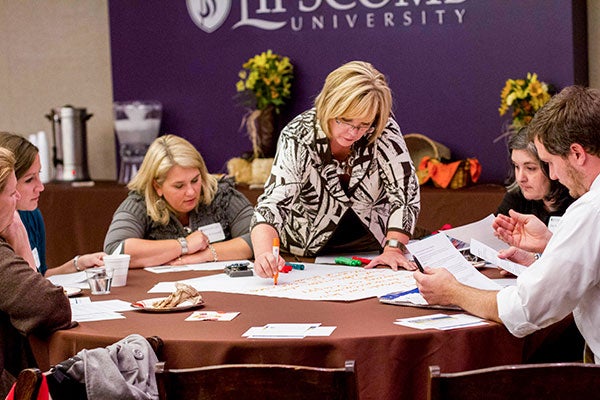 A group of teachers sit at a table while one records their discussion on a poster board