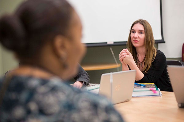 A woman looks toward and listens intently to another woman at a table