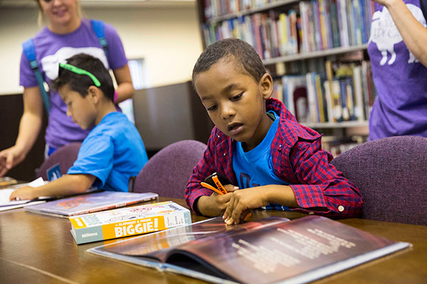 A young boy sits in a library and reads a book