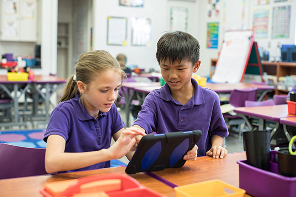 Two students sit together and use a tablet in the classroom