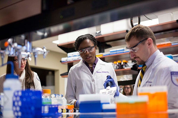 Pharmacy students stand at a lab bench conducting an experiment