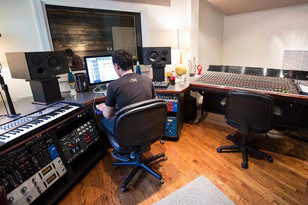 A student sits at a desktop on a audio editing software program in a music studio