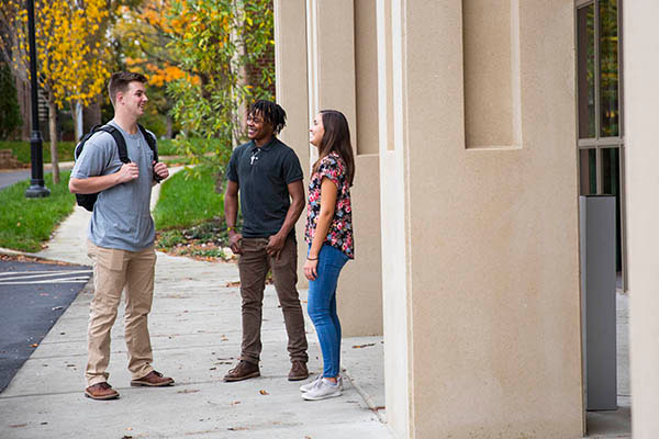 Three students stand outside talking