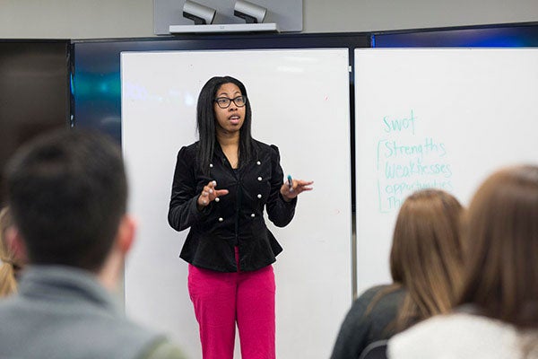 A professor stands before her class as she talks about a SWOT Analysis