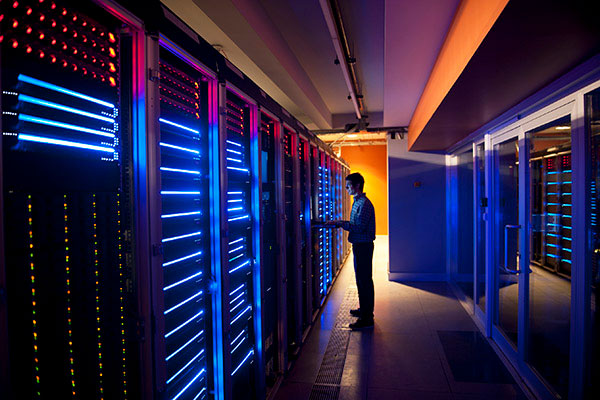 A man stands at a large computer server doing work