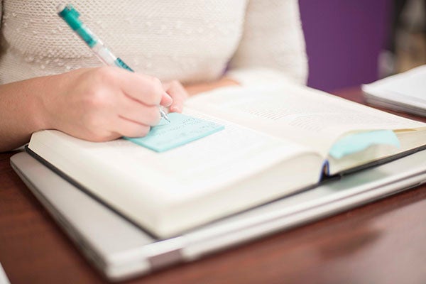 A student records notes on a Post-It as she reads a book