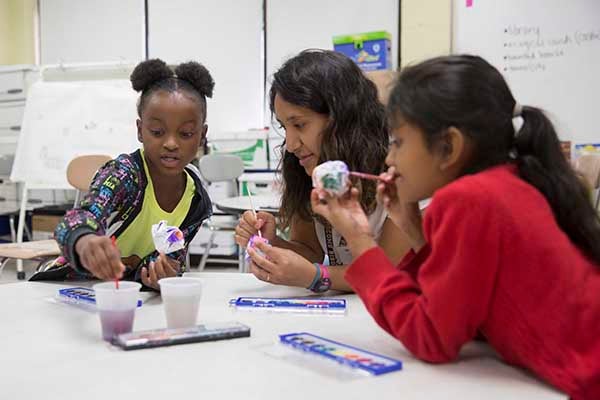 A college-aged female works with two children of different minority populations