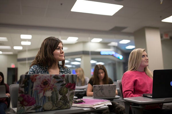 Two students sit in class ready to take notes while looking at their professor