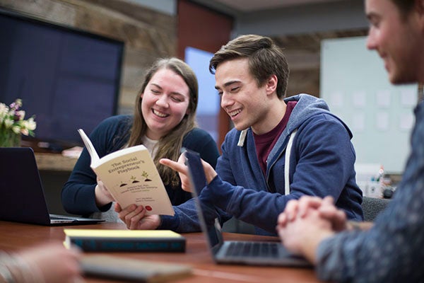 Two students read through their textbook titled "The Social Entrepreneur's Playbook"