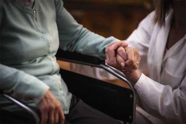 A woman holds hands with and elderly individual in a wheelchair