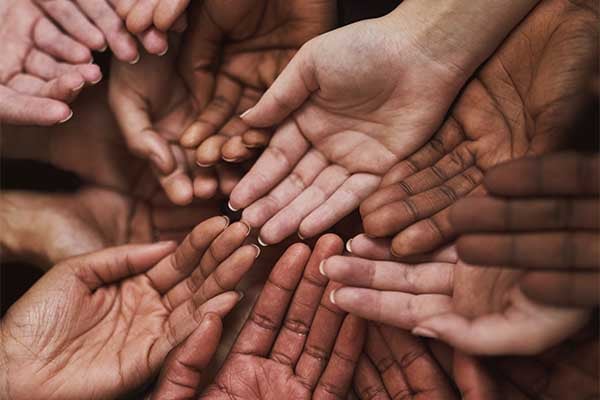 Multiple sets of hands of different colors with palms facing upwards reach toward one another