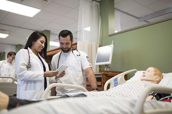 two students in lab coats with pretend patient