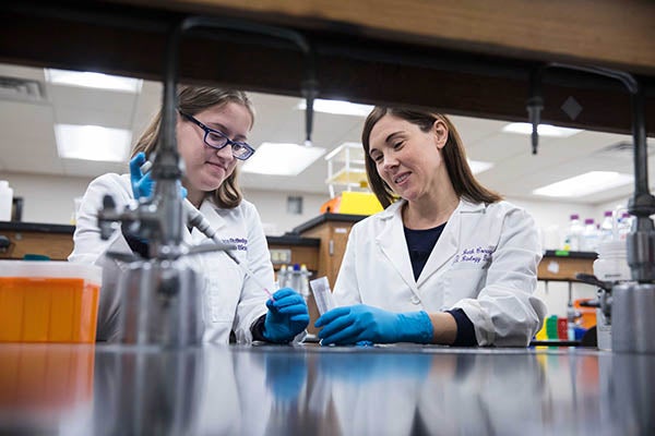 Two students in lab coats conduct an experiment at a lab bench