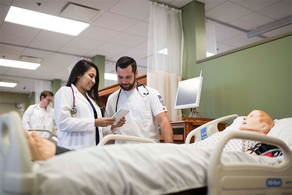 Nursing students reading a chart near a simulation mannequin.