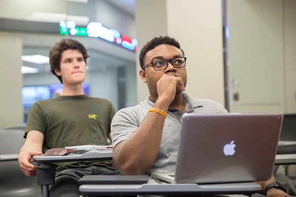 Two students sitting in classroom looking towards front of the room.