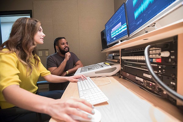 Two students work on producing a film together at a large desktop.