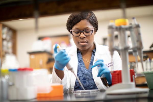 Female student uses pipette in lab.