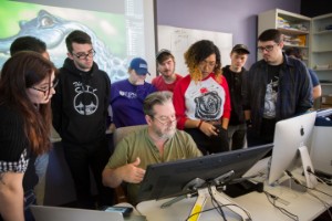 Animation teacher with group of students surrounding him looking at computer screen