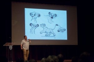 Man standing in front of screen with sketches of a lion projected onto it. 