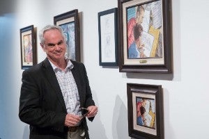 Man standing in front of wall with assortment of framed paintings