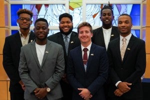 Six young men standing in front of a stained glass window