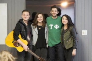 Four people standing and one holding a guitar