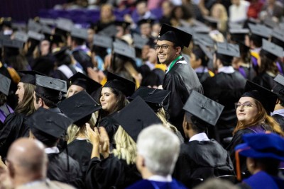 Graduate standing and smiling at ceremony when he sees parents. 
