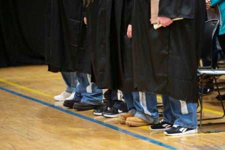 Graduates in prison blues with graduation robes covering them.