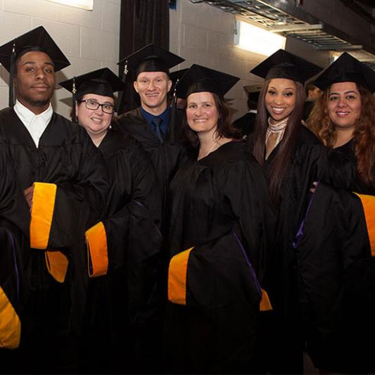 Students holding their regalia hoods line up before graduation ceremonies.