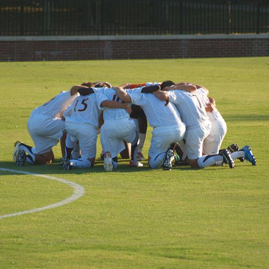 Men's soccer team huddles for prayer before a game.