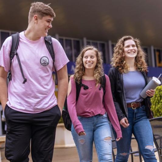 Three student smiling and walking across campus