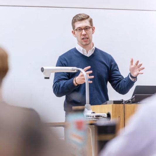 Professor teaching a class with a projector in front of him