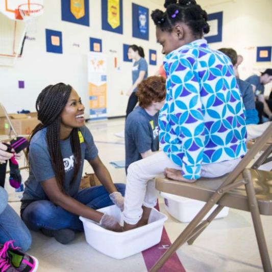 A student washing a littler girl's feet as part of Service Day