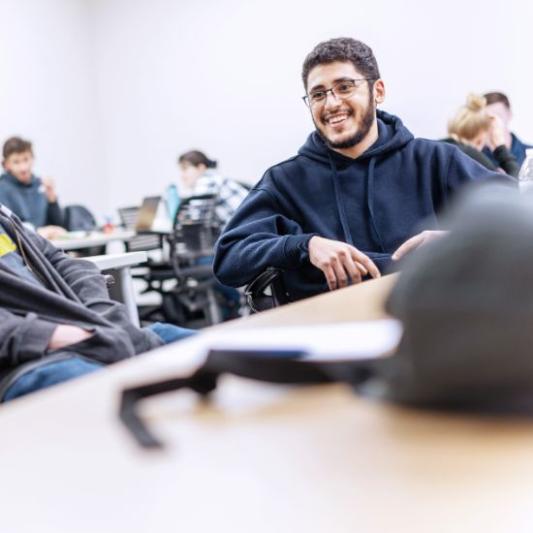 A male student smiling at his desk during class