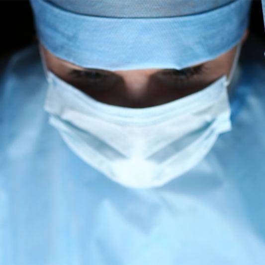 Physician assistant assists with surgery wearing blue scrubs and a mask.
