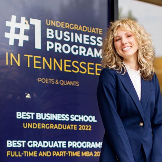 student standing next to the #1 undergraduate business program in tennessee sign